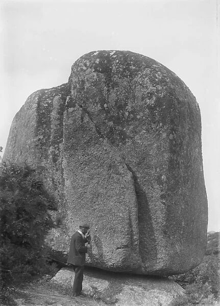 A man stands beside an enormous granite boulder, Luxulyan Valley, Cornwall. Probably 1900s