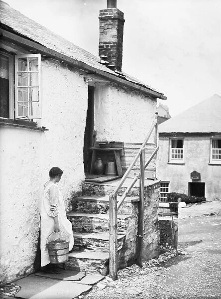 Teresa Mallett on cottage steps carrying a wooden barrel pail. Port Gaverne, St Endellion, Cornwall. 1906