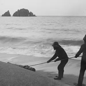 Two fishermen dragging a cannon across the tideline at Harlyn Bay, St Merryn, Cornwall. Probably early 1900s
