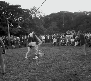 A crowd of people gathered to watch a Cornish wrestling match at an unknown location, Cornwall. 1970