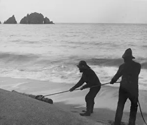 St Merryn Collection: Two fishermen dragging a cannon across the tideline at Harlyn Bay, St Merryn, Cornwall